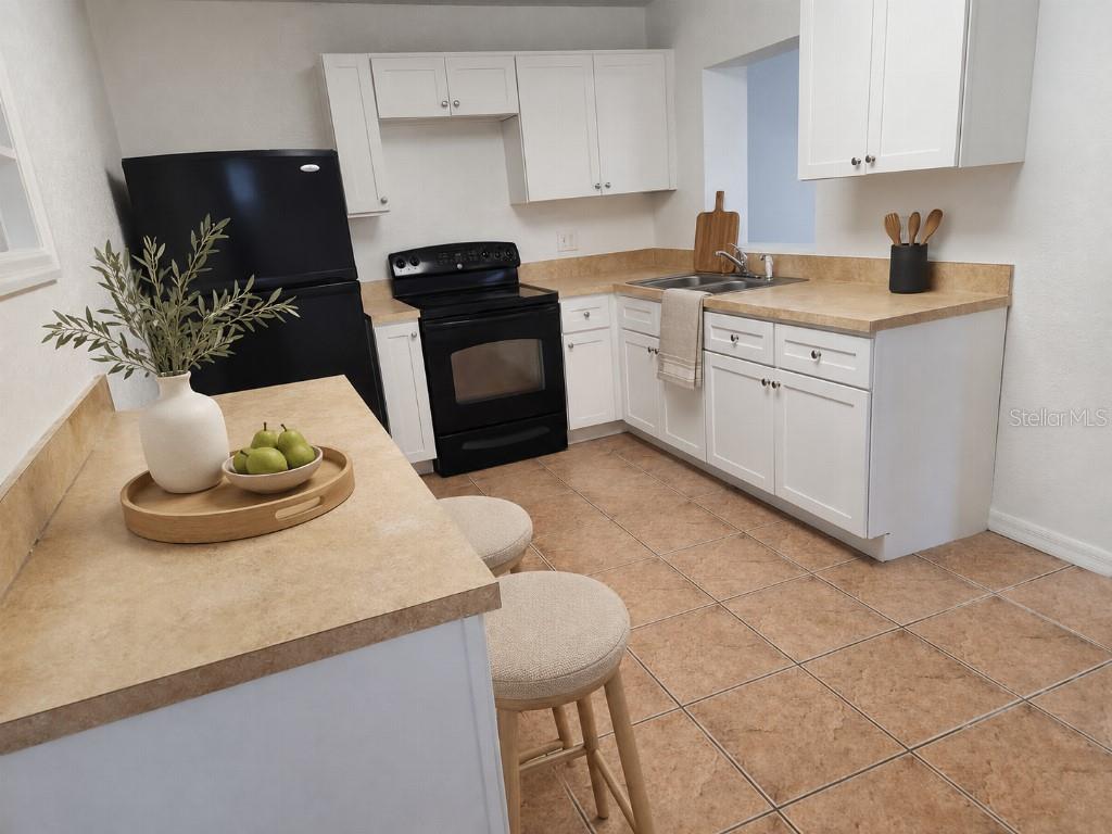 A kitchen features white cabinets, tan countertops, black appliances, and a small breakfast bar — 1005 N BRACEWELL DRIVE, PLANT CITY, FL