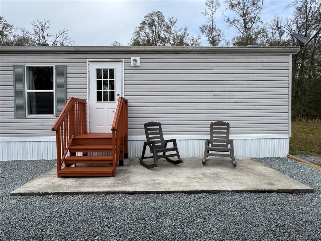 A gray mobile home exterior features a white door, wooden steps, and two rocking chairs — 4317 284TH STREET, BRANFORD, FL