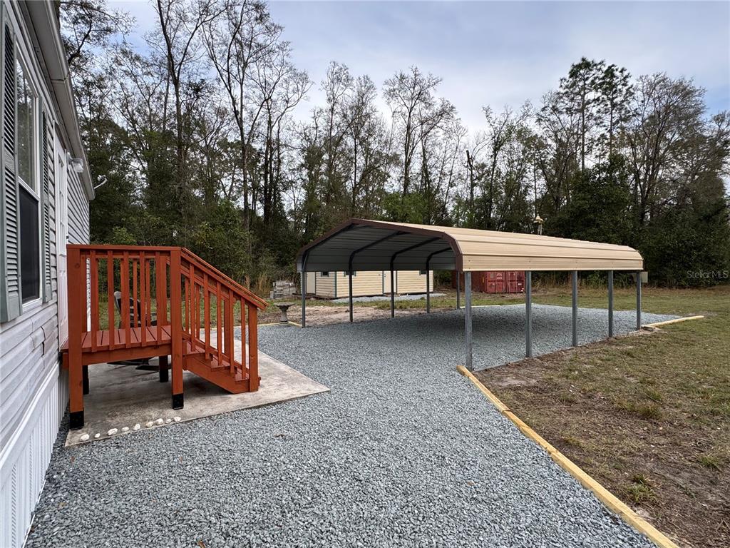 A gravel driveway features a metal carport next to a wooden deck and house exterior — 4317 284TH STREET, BRANFORD, FL