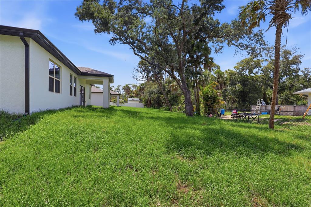 A grassy backyard view of a house exterior with a covered patio and large trees — 4844 FLINT DRIVE, NORTH PORT, FL