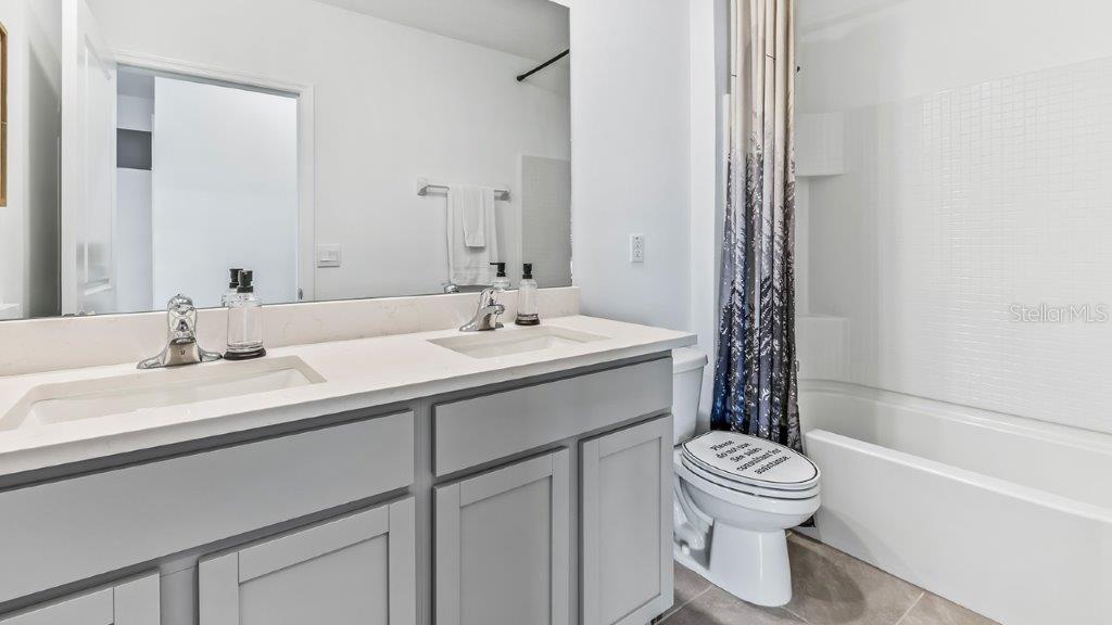 A bathroom features a double vanity with gray cabinets, white countertops, and a shower-tub combo — 17950 ACORN DROP ROAD, LAND O LAKES, FL
