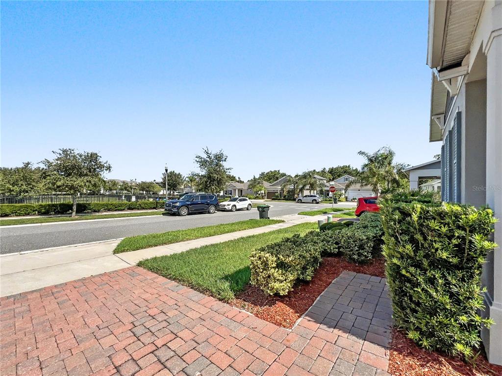 A view from a brick-paved walkway looking toward a suburban street with parked cars — 1808 WESTERN TRAILWAY DRIVE, WINTER GARDEN, FL
