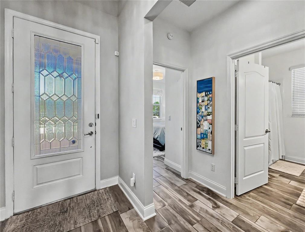 A white front door with decorative glass opens into a hallway with wood-look tile flooring — 1808 WESTERN TRAILWAY DRIVE, WINTER GARDEN, FL