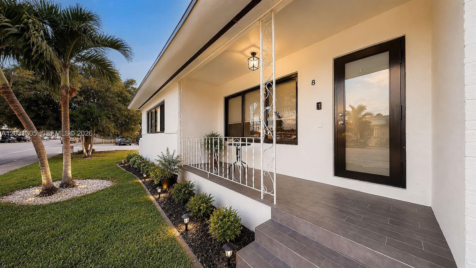 A white house exterior features a tiled front porch, black door, and decorative metal railing — 101 W 11th St # 8, Hialeah FL 33010, HIALEAH, FL