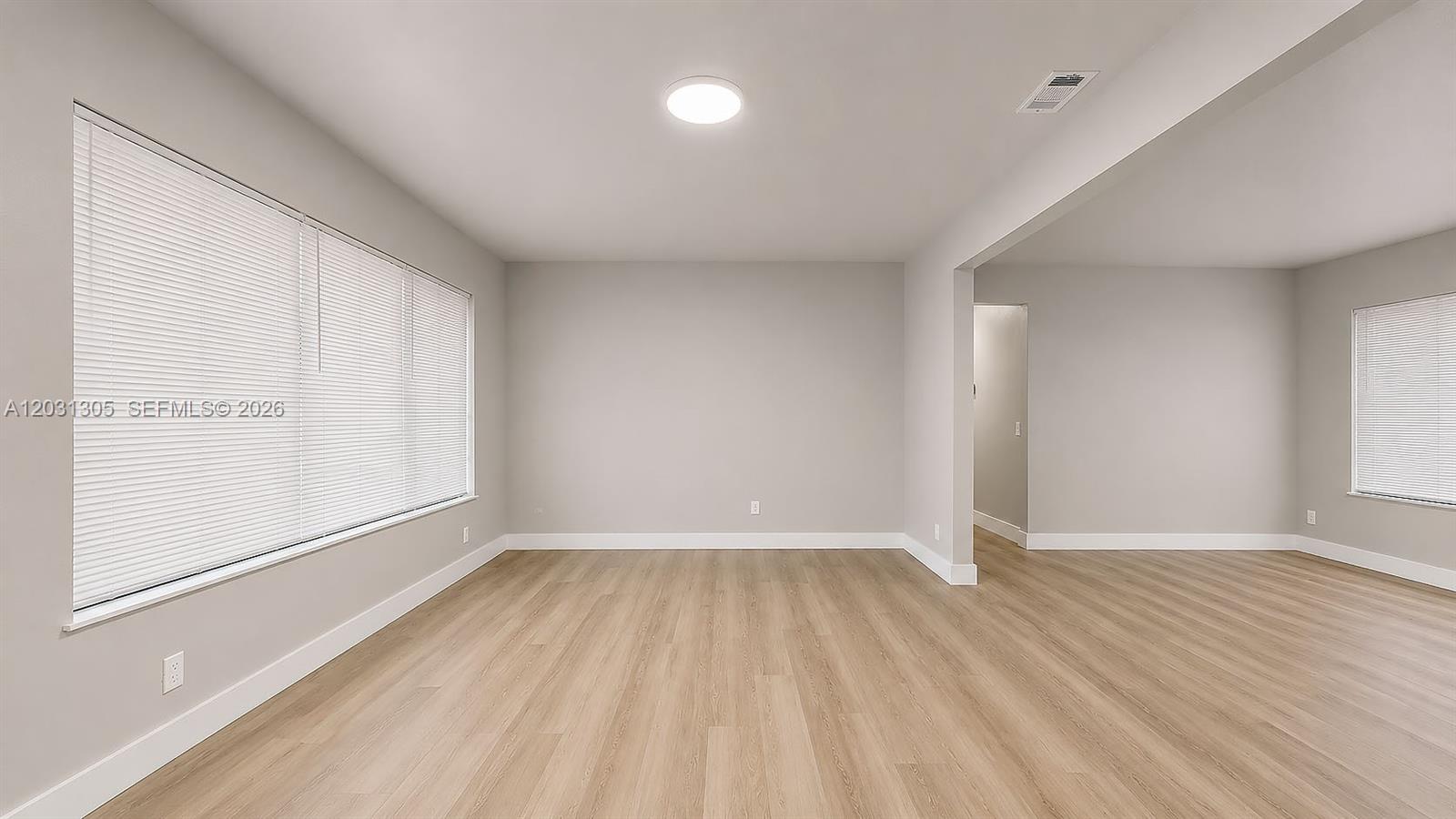 This empty room features light wood-look flooring, neutral walls, and large windows with blinds — 101 W 11th St # 8, Hialeah FL 33010, HIALEAH, FL