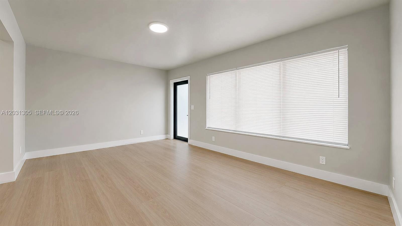 An empty room features light-colored wood-look flooring, light gray walls, and a large window — 101 W 11th St # 8, Hialeah FL 33010, HIALEAH, FL