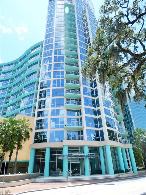 A tall, modern glass-and-concrete high-rise building with turquoise accents and balconies under a blue sky — 322 E CENTRAL BOULEVARD UNIT 1104, ORLANDO, FL