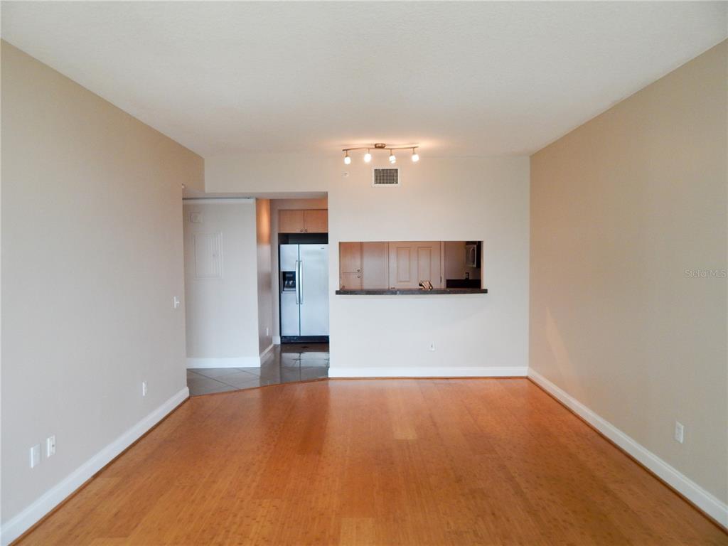 An empty living room with hardwood floors features a pass-through window to the kitchen — 322 E CENTRAL BOULEVARD UNIT 1104, ORLANDO, FL