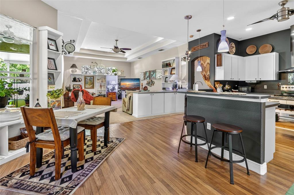 An open-concept kitchen and dining area features hardwood floors, white cabinetry, and a breakfast bar — 13189 JESSICA DRIVE, SPRING HILL, FL