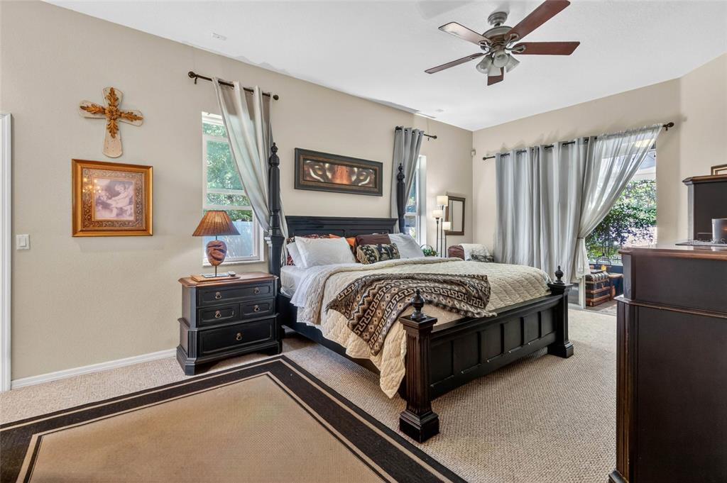 A bedroom features a dark wood four-poster bed, beige carpet, and large windows with curtains — 13189 JESSICA DRIVE, SPRING HILL, FL