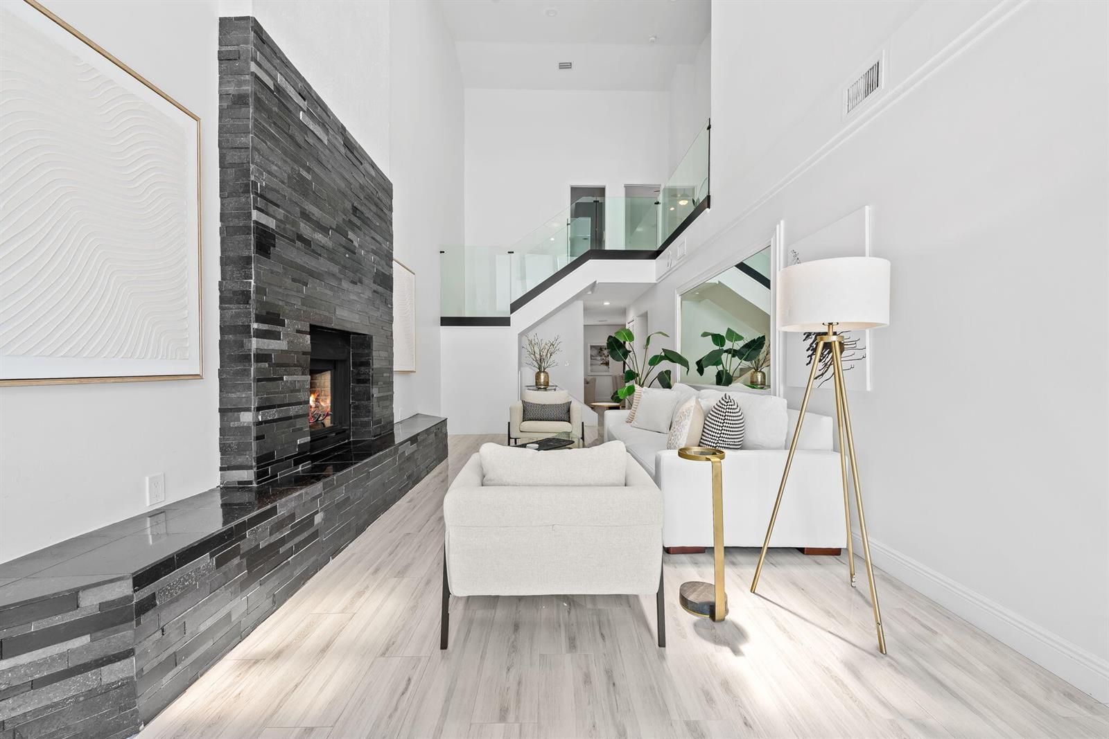 A living room features a tall black stone fireplace, white furniture, and a glass-railed staircase — 2930 Florida Boulevard, Delray Beach FL 33483, DELRAY BEACH, FL