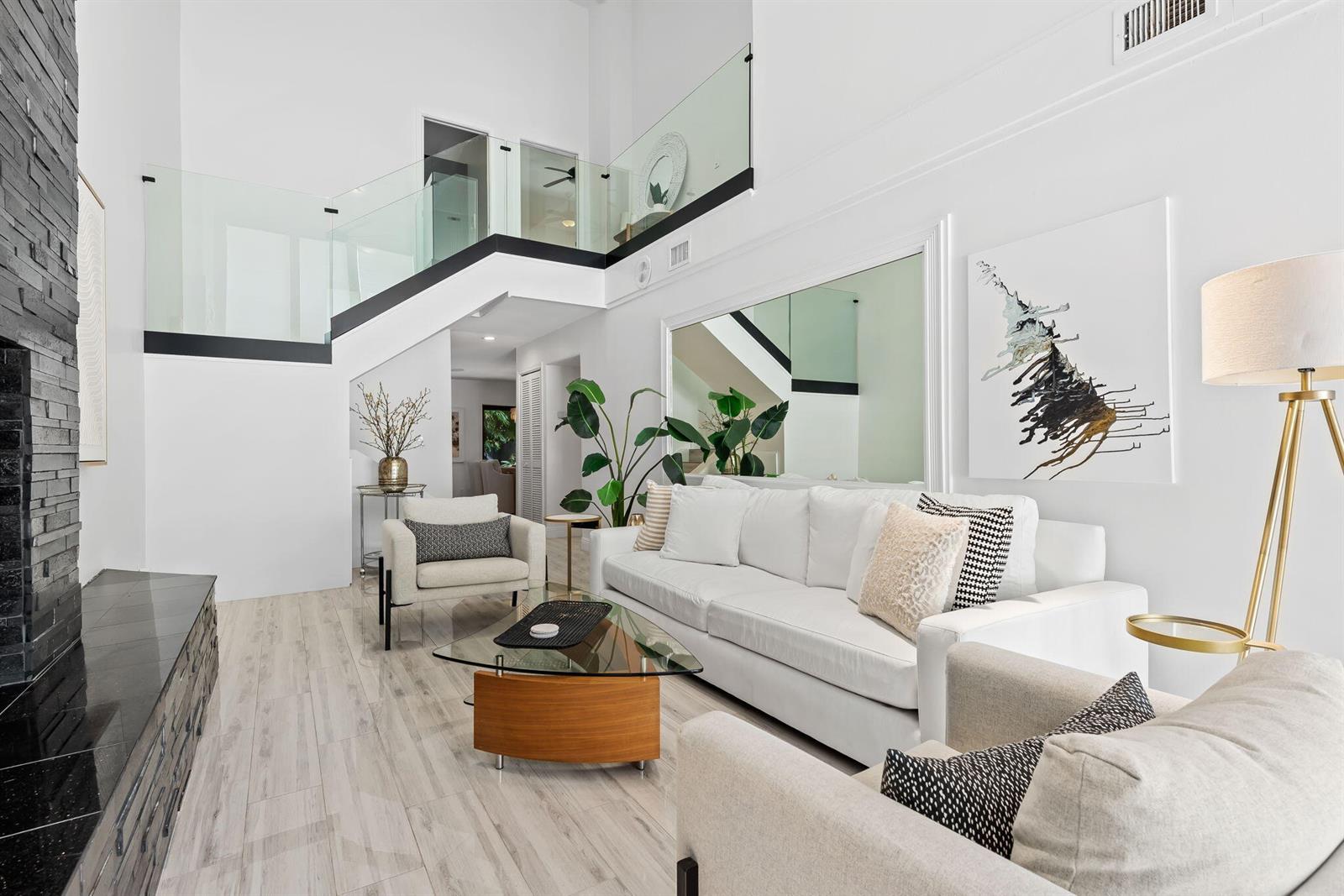 A modern living room features a white sofa, glass coffee table, and a glass-railed staircase — 2930 Florida Boulevard, Delray Beach FL 33483, DELRAY BEACH, FL