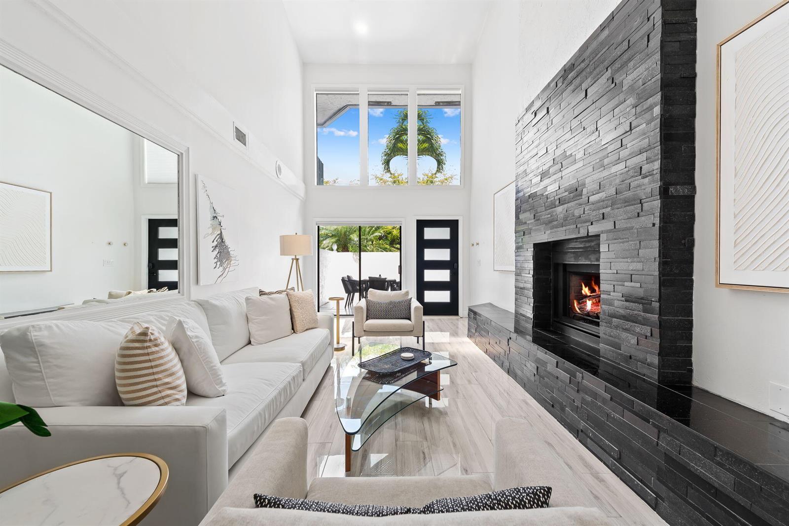 A modern living room features a tall black stone fireplace, white sofa, and floor-to-ceiling windows — 2930 Florida Boulevard, Delray Beach FL 33483, DELRAY BEACH, FL