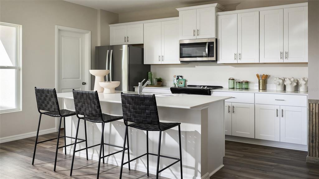 A modern kitchen features white cabinets, stainless steel appliances, a central island, and black barstools — 9150 BENT BRANCH, DADE CITY, FL