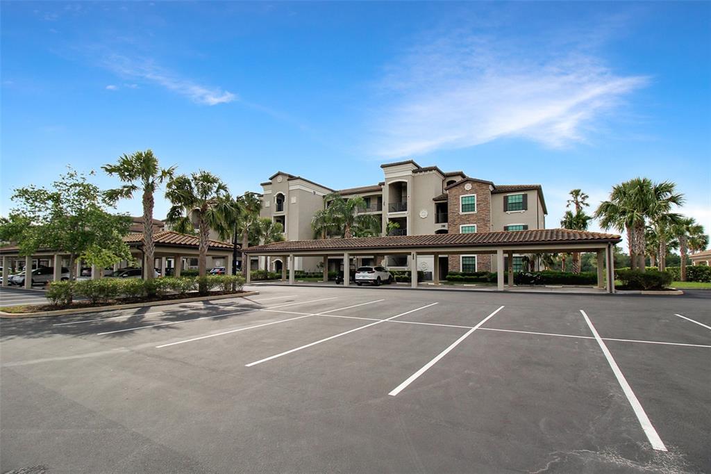 An apartment building with a covered parking area and palm trees under a blue sky — 17006 VARDON TERRACE UNIT 406, BRADENTON, FL