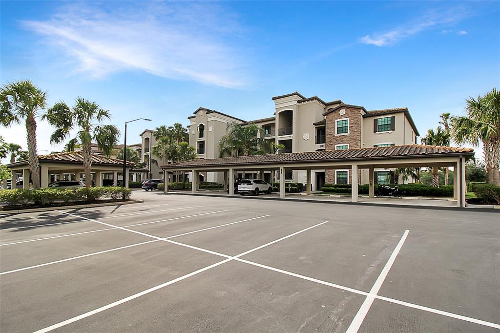 An apartment building exterior with covered parking spaces and palm trees in a parking lot — 17006 VARDON TERRACE UNIT 406, BRADENTON, FL