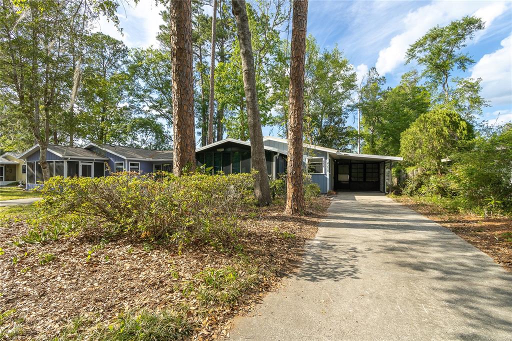 A single-story house with a carport and screened porch sits behind a wooded front yard — 4224 NW 87TH LANE, GAINESVILLE, FL