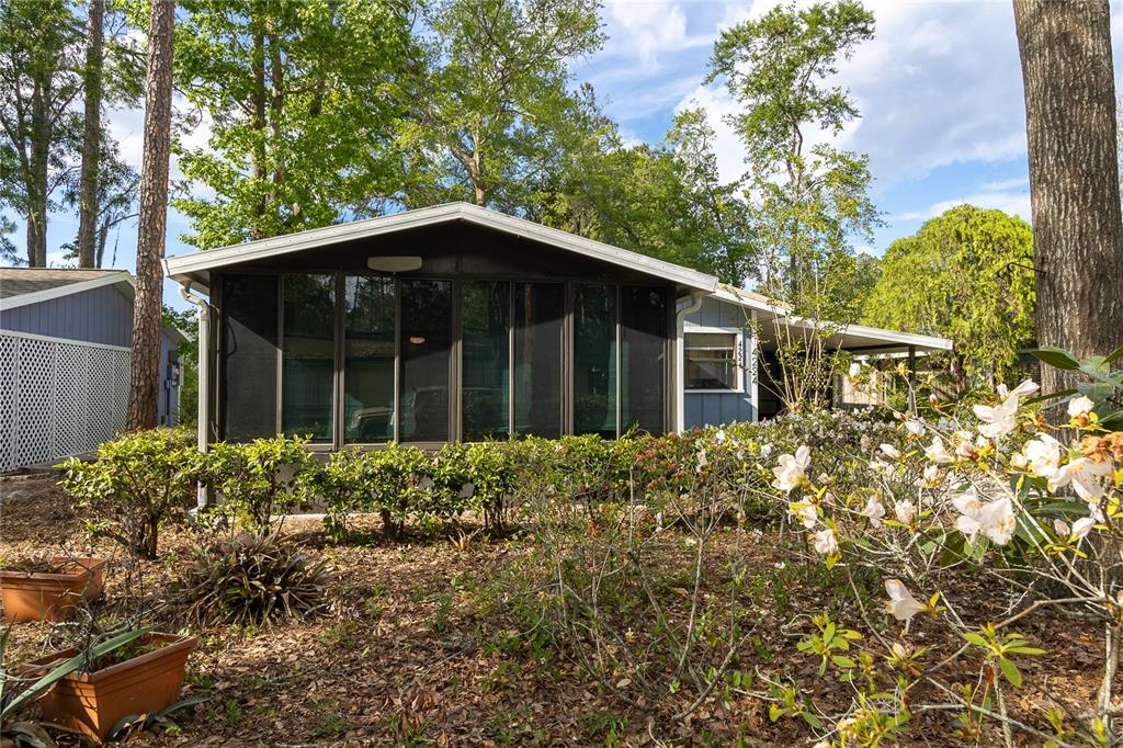 A single-story house with a screened-in porch sits among trees and flowering bushes — 4224 NW 87TH LANE, GAINESVILLE, FL
