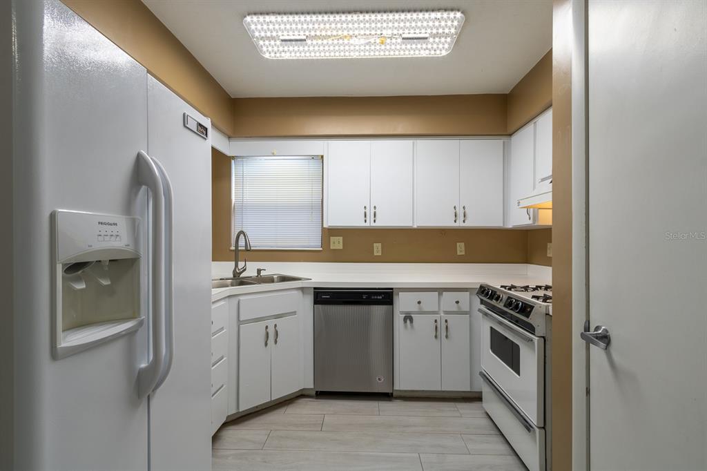 A kitchen features white cabinets, stainless steel appliances, tan walls, and light-colored wood-look flooring — 4224 NW 87TH LANE, GAINESVILLE, FL