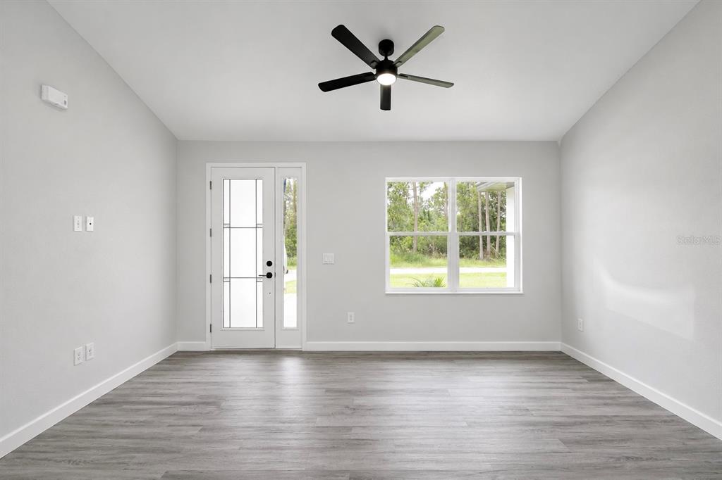 A living room with light gray walls, wood-look flooring, a ceiling fan, and a front door — 6523 ORDUNA DRIVE, SEBRING, FL