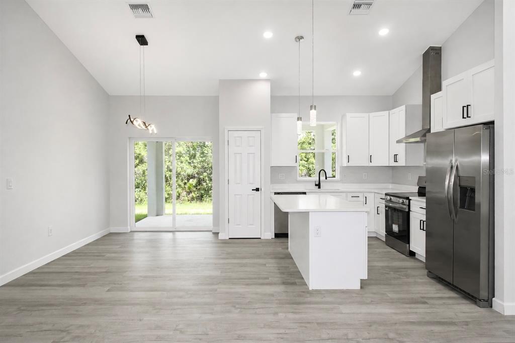 A modern kitchen with white cabinets, stainless steel appliances, and an island opens to a patio — 6523 ORDUNA DRIVE, SEBRING, FL