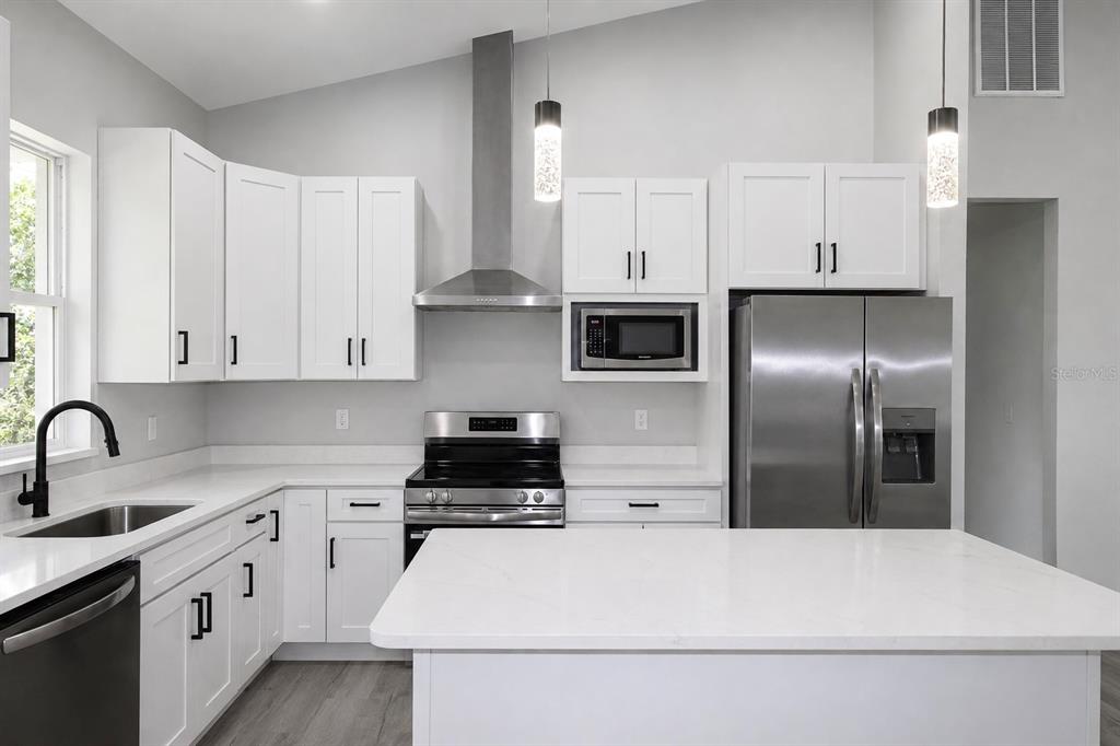 A modern kitchen features white cabinets, stainless steel appliances, a kitchen island, and quartz countertops — 6523 ORDUNA DRIVE, SEBRING, FL