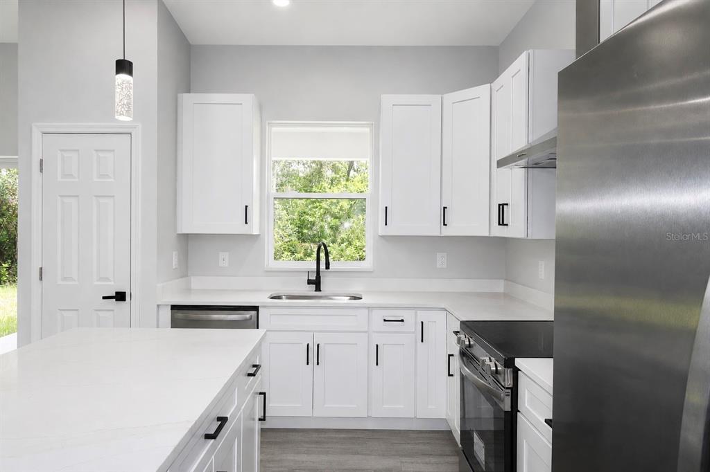 A modern kitchen features white cabinets, stainless steel appliances, and a large quartz island — 6523 ORDUNA DRIVE, SEBRING, FL