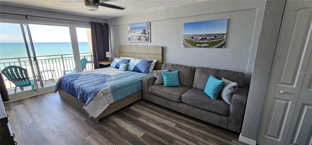 A bedroom with a bed and sofa features wood-look flooring and a balcony overlooking the ocean — 219 S ATLANTIC AVENUE UNIT 412, DAYTONA BEACH, FL