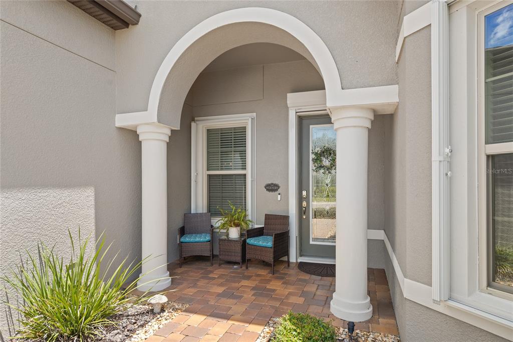 A covered front porch features a brick paver floor, two wicker chairs, and arched columns — 4792 MARITIME WATERS COURT, LAND O LAKES, FL