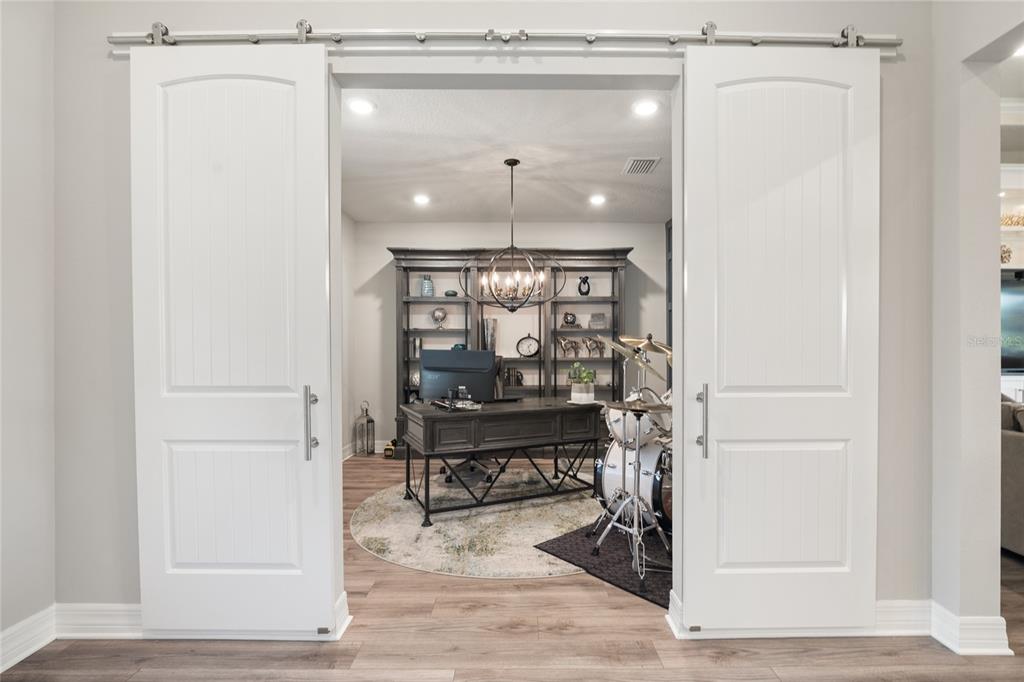 A home office with a desk, bookshelf, and drum set viewed through white sliding barn doors — 4792 MARITIME WATERS COURT, LAND O LAKES, FL