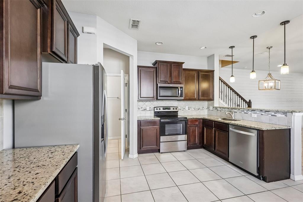 A kitchen with dark wood cabinets, granite countertops, stainless steel appliances, and light tile flooring — 1164 PAVIA DRIVE, APOPKA, FL
