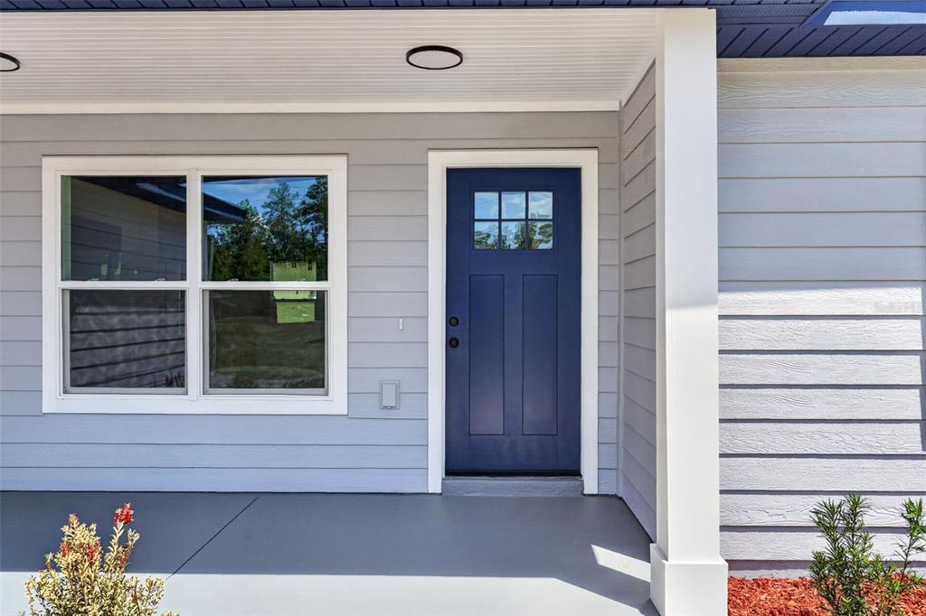 A blue front door with a window sits on a gray-sided porch with a column — 16856 SW 43RD COURT ROAD, OCALA, FL