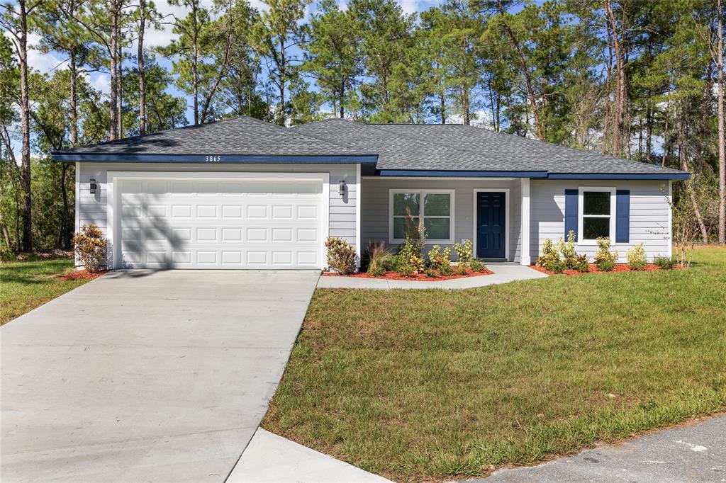 A single-story house with gray siding, a white garage door, and a dark blue door — 16856 SW 43RD COURT ROAD, OCALA, FL