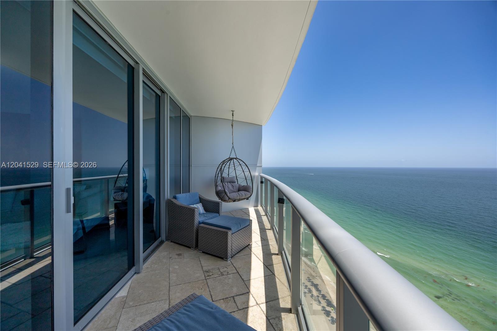 A balcony with stone flooring, wicker furniture, a hanging chair, and ocean views — SUNNY ISLES BEACH, FL