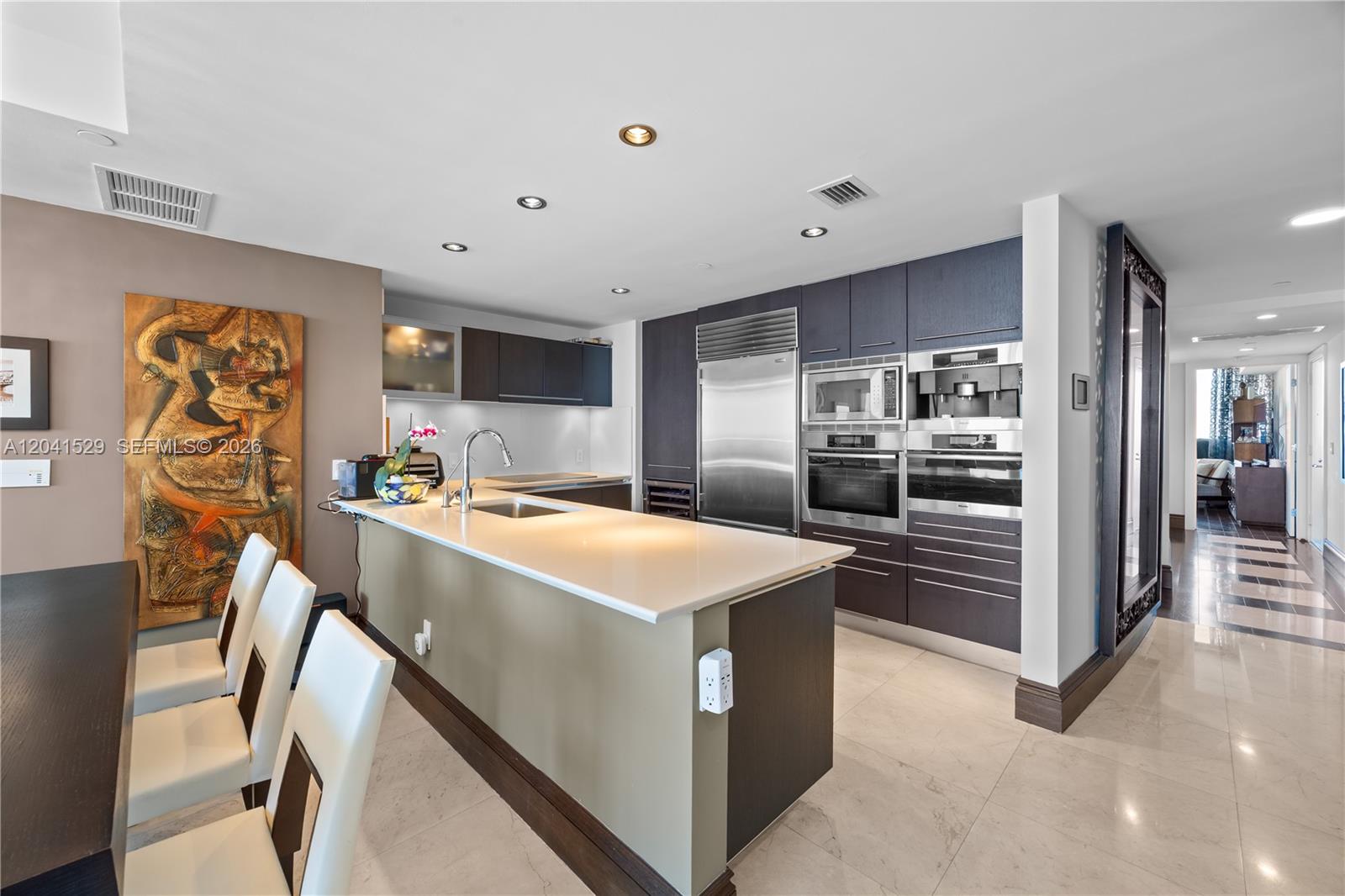 A modern kitchen features dark cabinetry, stainless steel appliances, and a central island with seating — SUNNY ISLES BEACH, FL