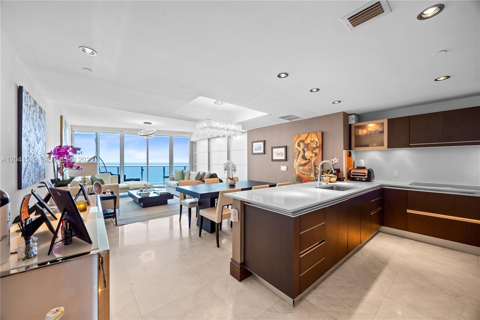A modern open-concept kitchen and living area features dark wood cabinetry, white countertops, and ocean views — SUNNY ISLES BEACH, FL