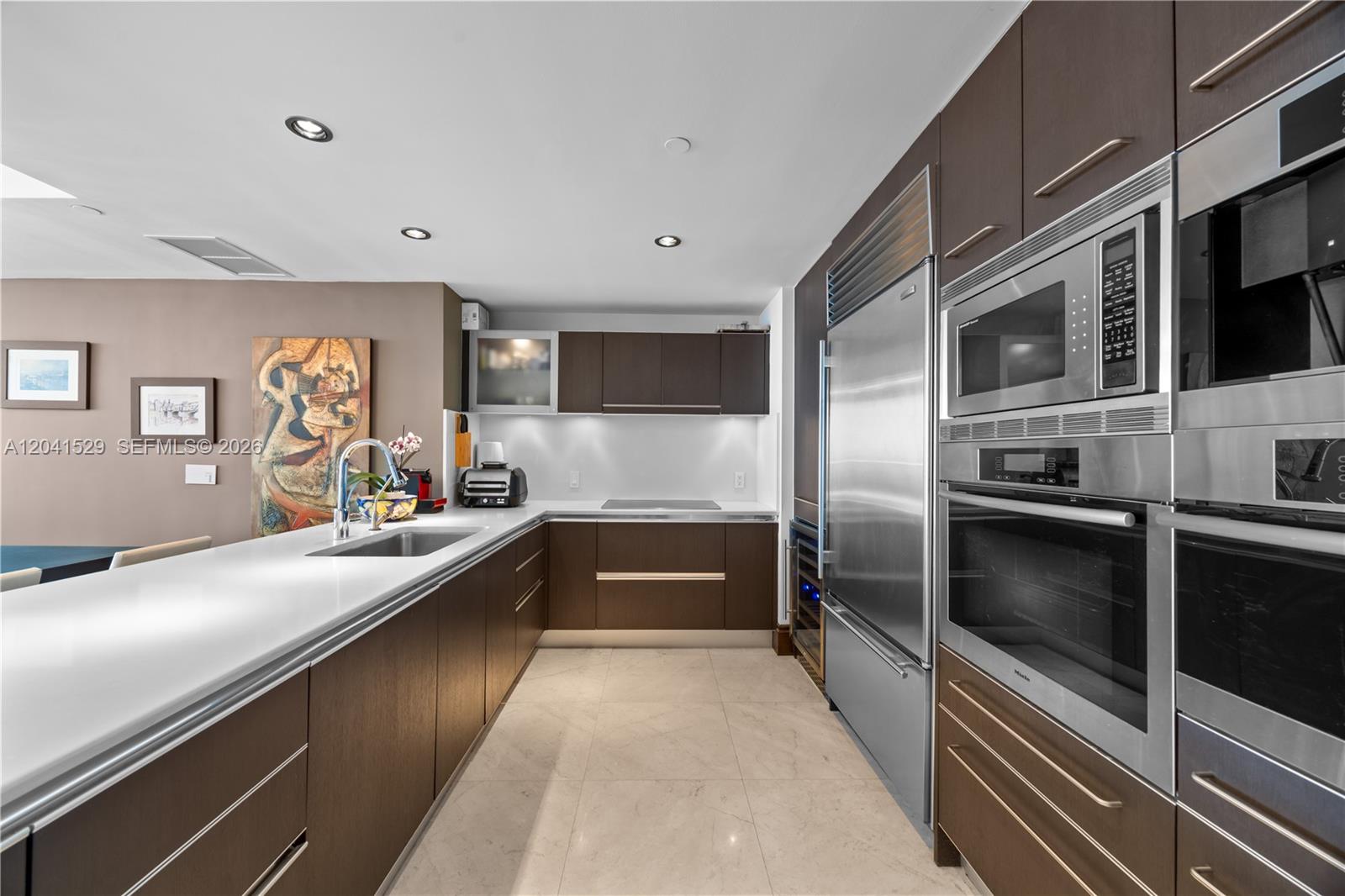 A modern kitchen features dark wood cabinetry, stainless steel appliances, and white countertops — SUNNY ISLES BEACH, FL
