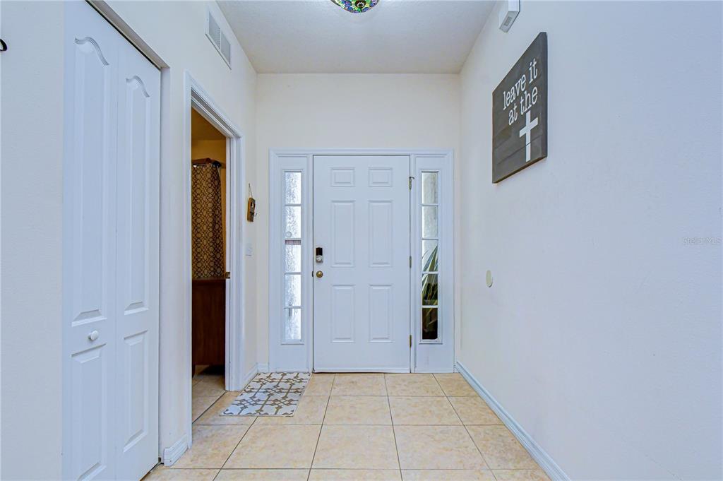 A red front door with a cross decoration sits at the end of a covered entryway — 6252 TWIN BRIDGES DRIVE, ZEPHYRHILLS, FL