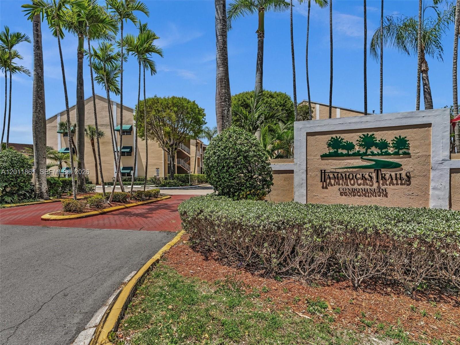 A sign for Hammocks Trails Condominium stands near a paved entrance with palm trees — 15325 SW 106th Ter # 636, Miami FL 33196, MIAMI, FL