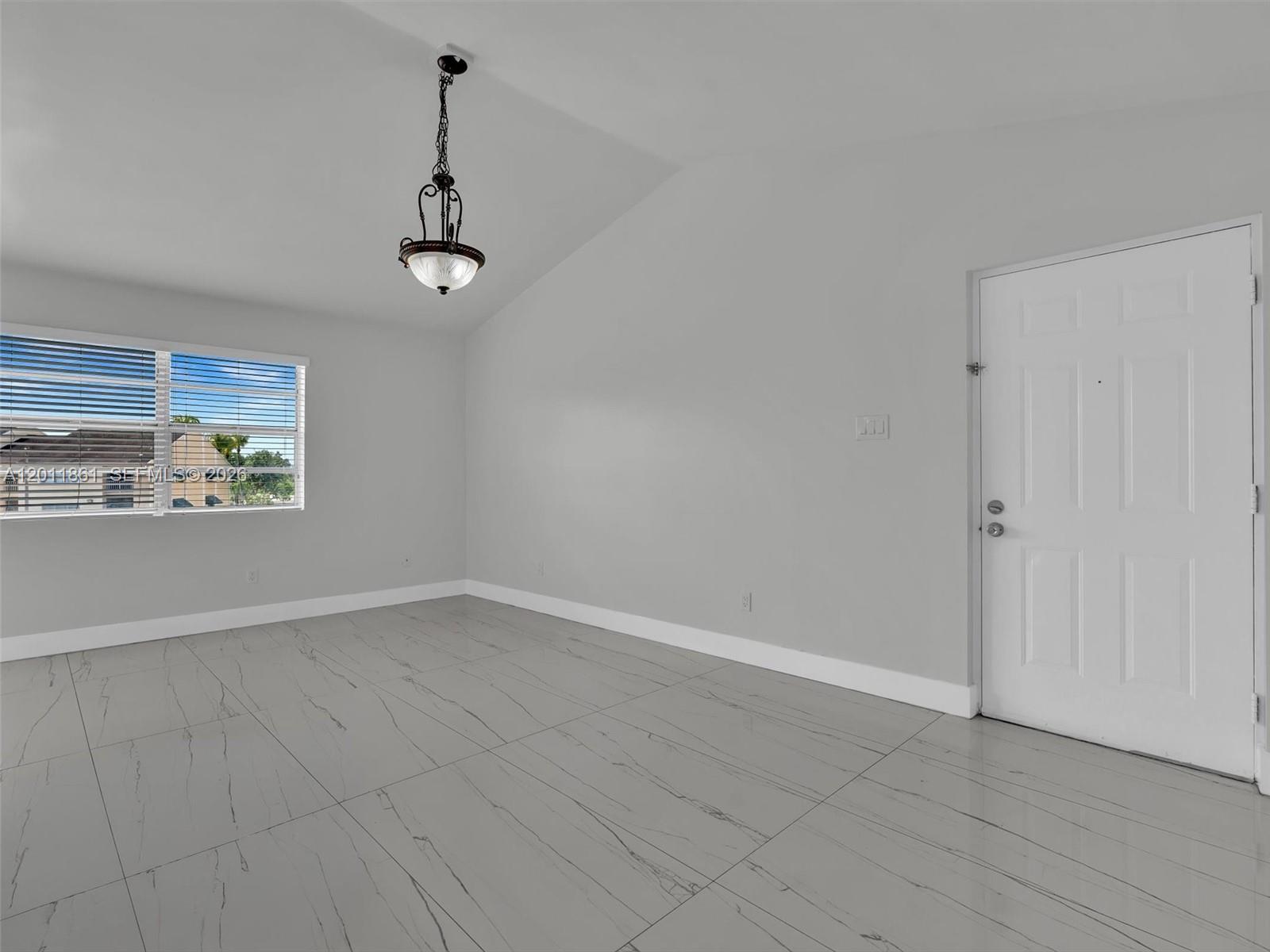 An empty room features light gray walls, white tile flooring, a window, and a hanging light — 15325 SW 106th Ter # 636, Miami FL 33196, MIAMI, FL