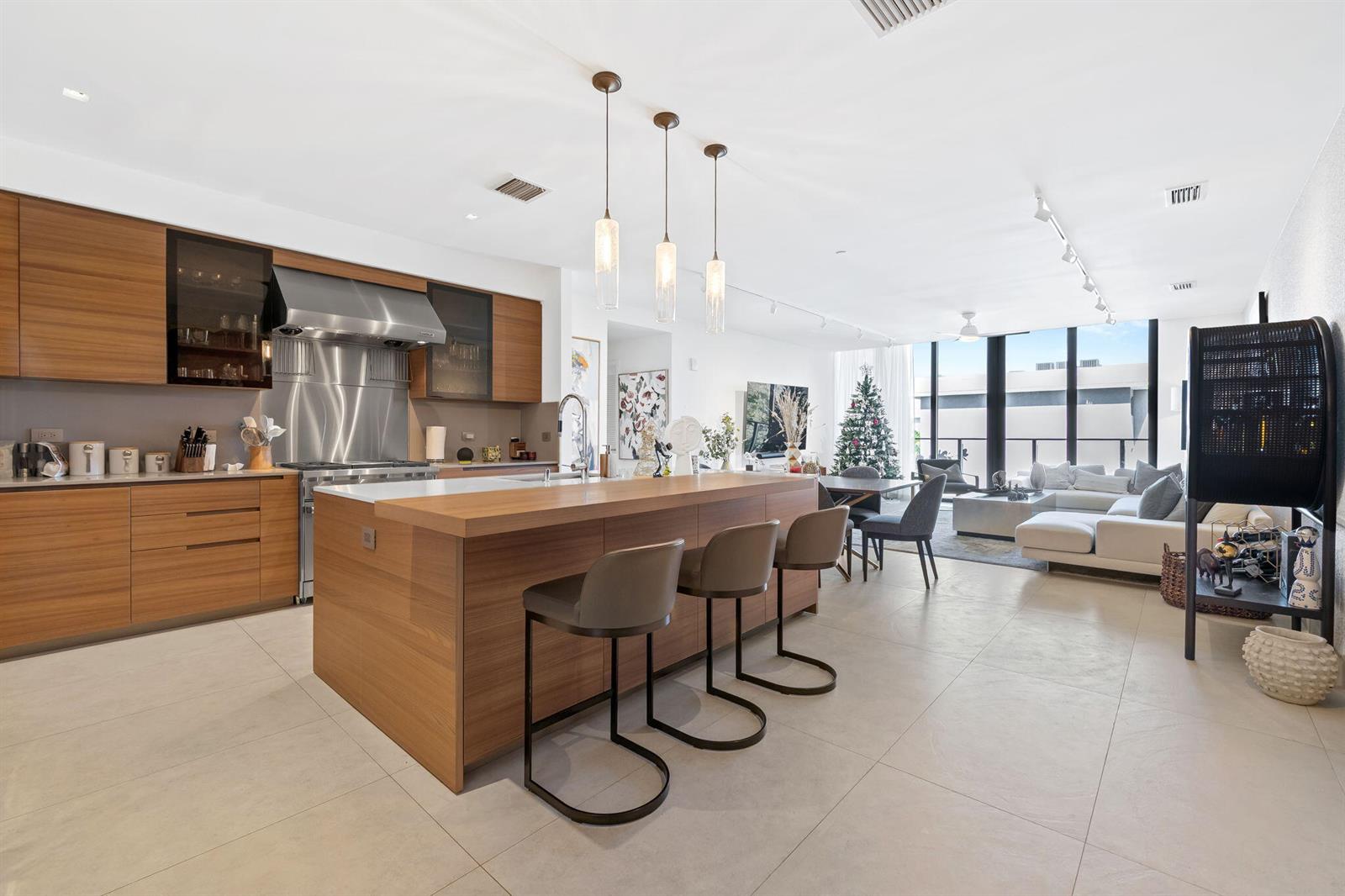 A modern open-concept kitchen features wood cabinetry, a large island with bar stools, and living area — 3581 E Glencoe Street # 408, Miami FL 33133, MIAMI, FL