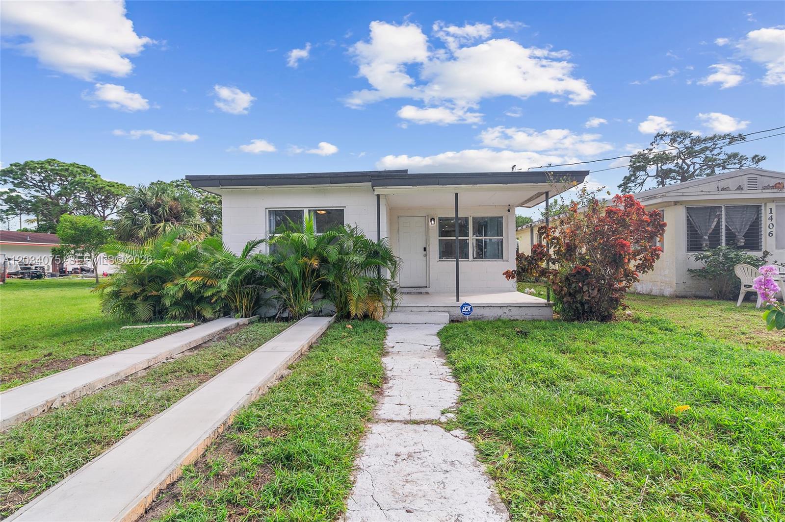 A single-story white house with a flat roof, a front porch, and a concrete driveway — 1408 N 23rd St, Fort Pierce FL 34950, FORT PIERCE, FL