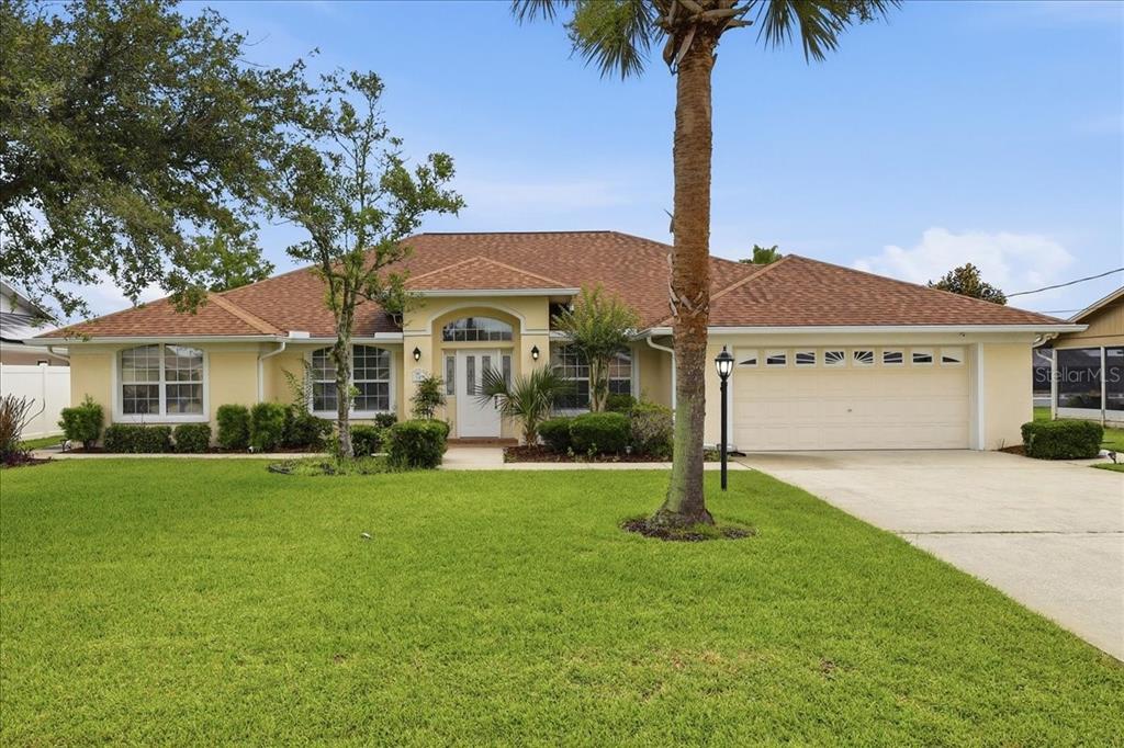 A single-story house with a beige stucco exterior, a brown shingled roof, and a palm tree — 36 CLOVERDALE COURT N, PALM COAST, FL