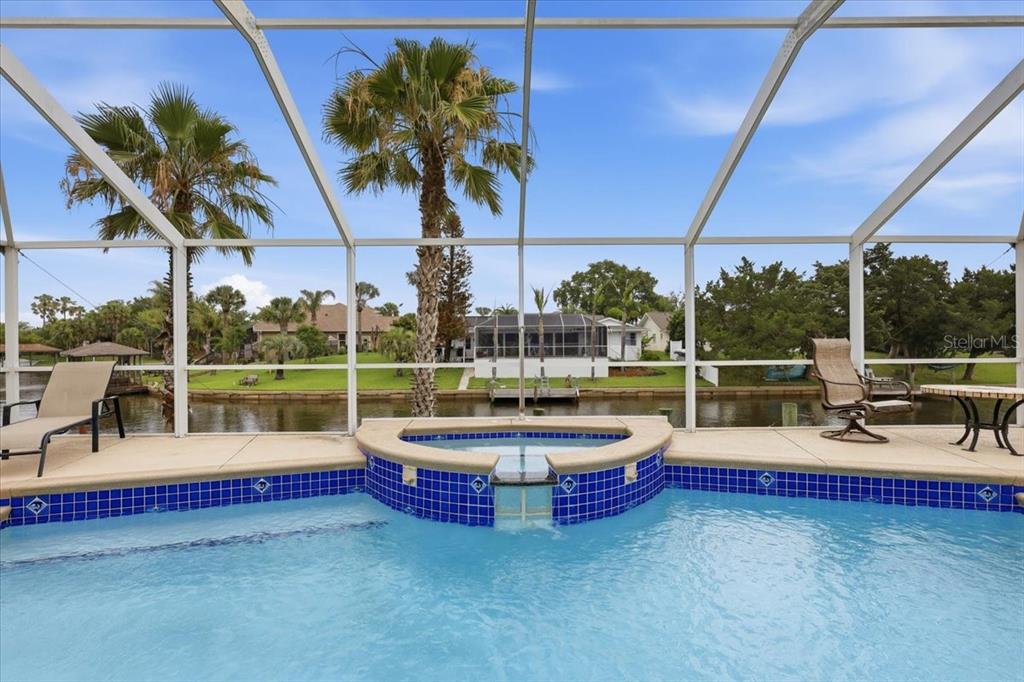 A swimming pool and spa are enclosed by a screen cage overlooking a canal — 36 CLOVERDALE COURT N, PALM COAST, FL