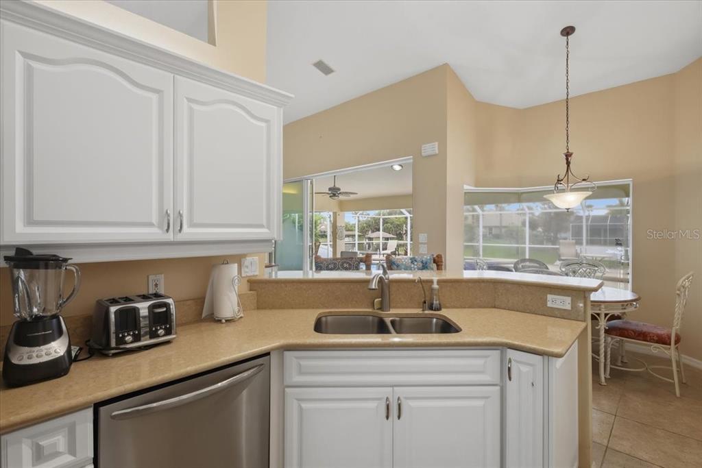 A kitchen features white cabinets, tan countertops, a double sink, and a view of a patio — 36 CLOVERDALE COURT N, PALM COAST, FL
