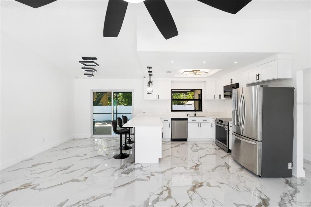 A modern kitchen features white cabinetry, stainless steel appliances, a center island, and marble-patterned tile flooring — 3823 E NORFOLK STREET, TAMPA, FL