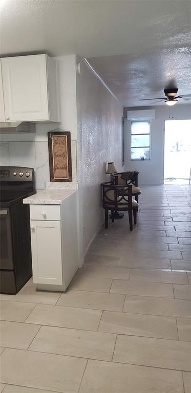 A kitchen with white cabinets and a black stove opens into a tiled living area — 1118 HARRIS LANE, CLEARWATER, FL