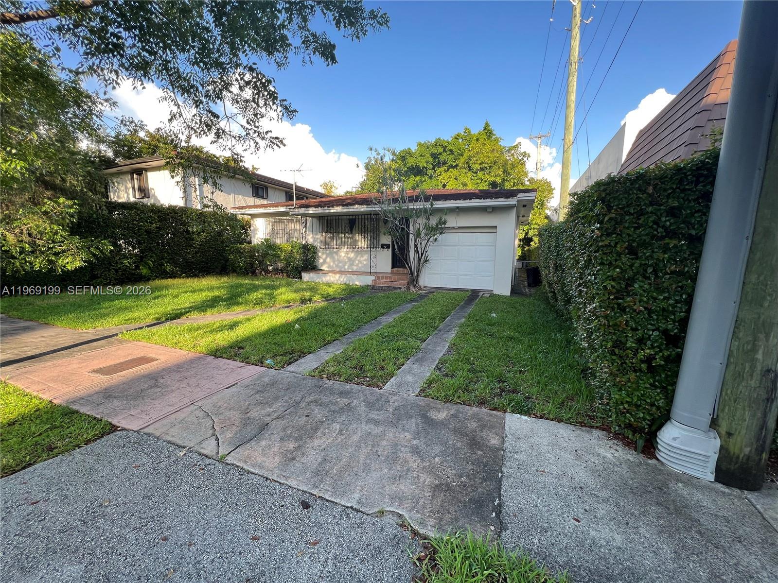 A single-story house features a white garage, a concrete driveway, and a manicured hedge — 812 Columbus Blvd, Coral Gables FL 33134, CORAL GABLES, FL