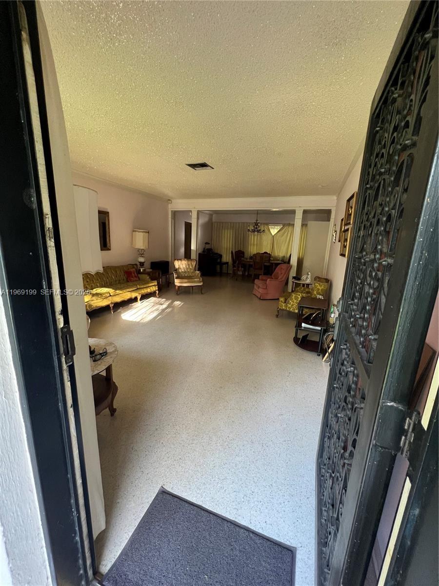 A view through a doorway into a living room with terrazzo flooring and vintage furniture — 812 Columbus Blvd, Coral Gables FL 33134, CORAL GABLES, FL
