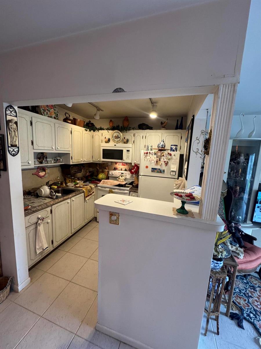 A kitchen with white cabinets, tile flooring, and a breakfast bar opening to a living area — 90 South Boulevard # 1c, Boynton Beach FL 33435, BOYNTON BEACH, FL